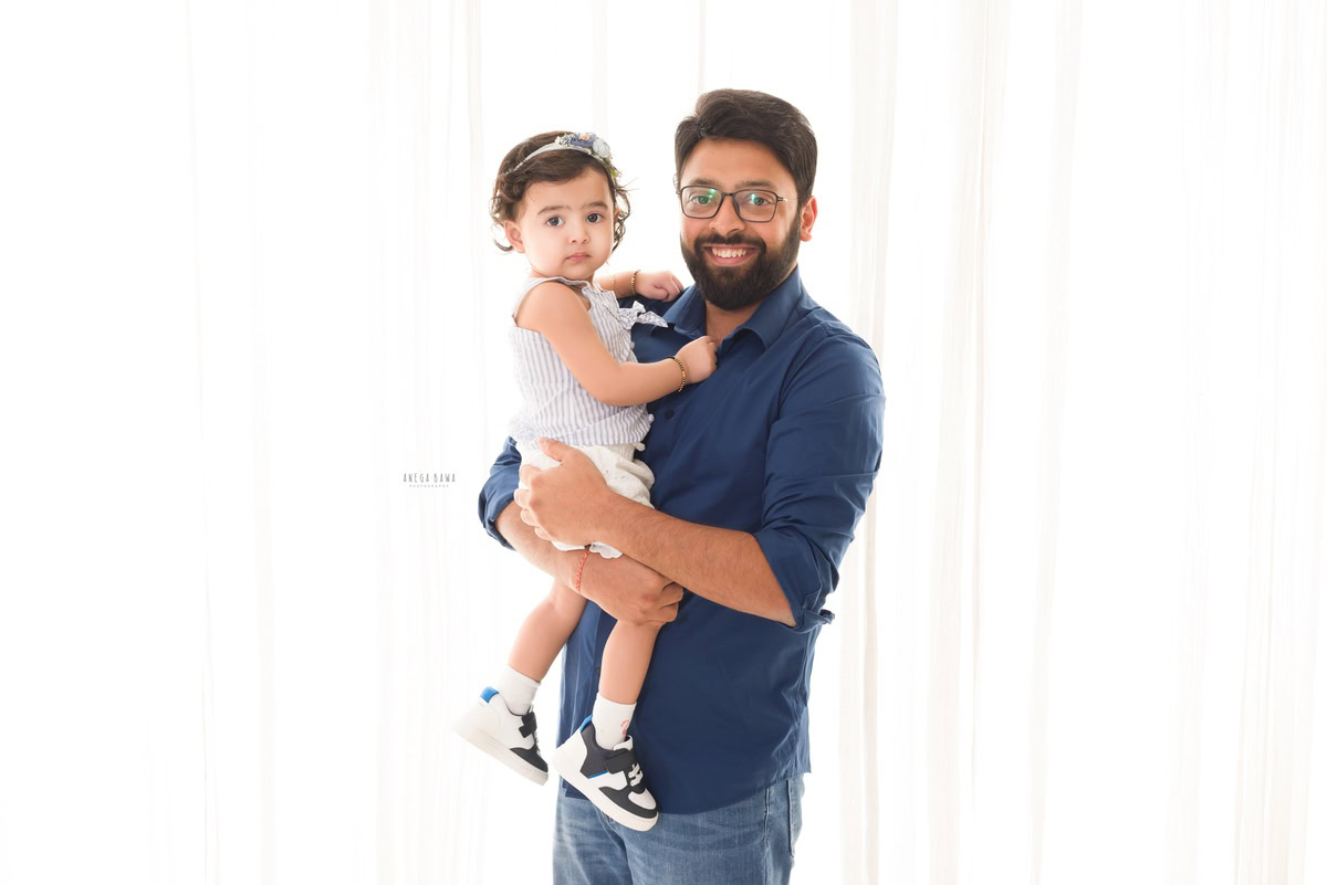 10-months girl posing with dad in a cute headband against a white backdrop, captured by Anega Bawa Family Photographer in Gurgaon (Delhi NCR).