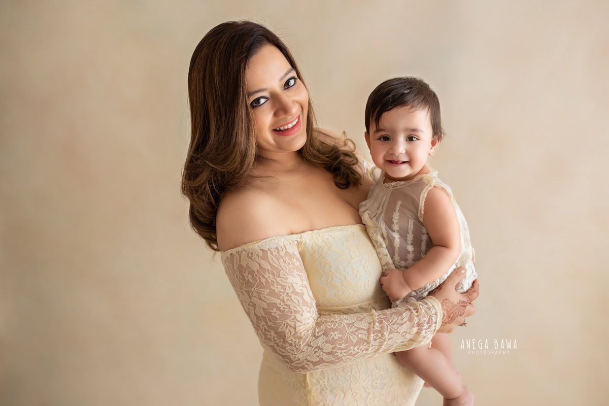 10-month-old girl posing with mom in a beige dress, against a complementary beige backdrop, in a charming family portrait by Anega Bawa, Gurgaon (Delhi, NCR)