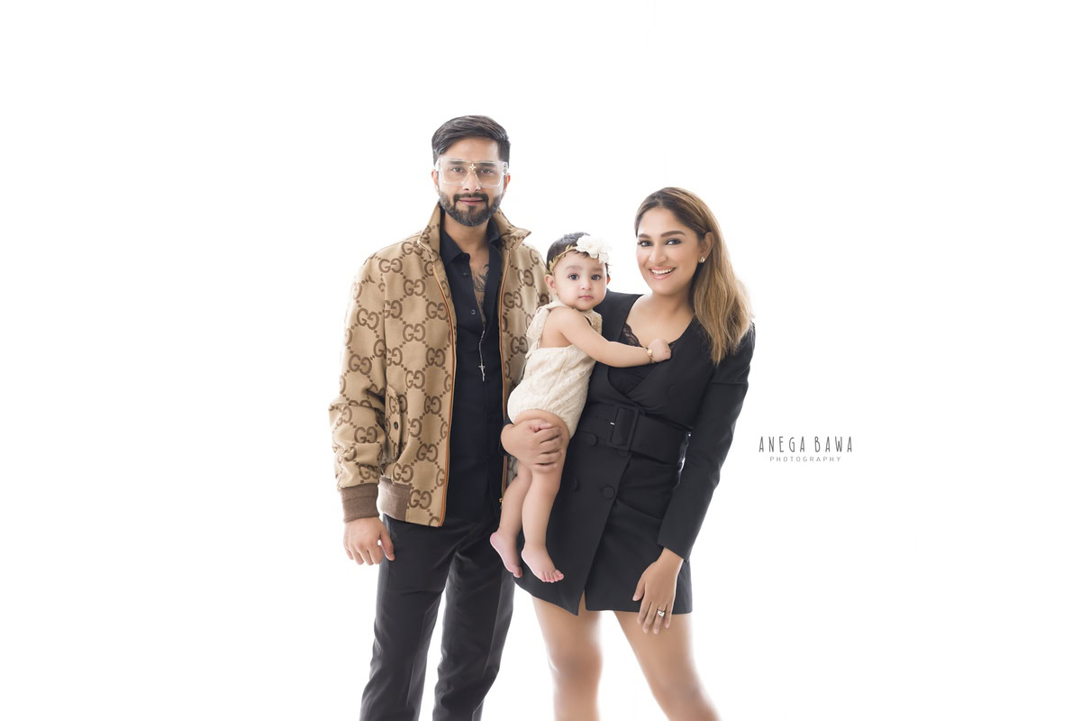 10-month-old girl posing with mom and dad against a soft beige backdrop, captured beautifully by Anega Bawa in Gurgaon (Delhi, NCR)