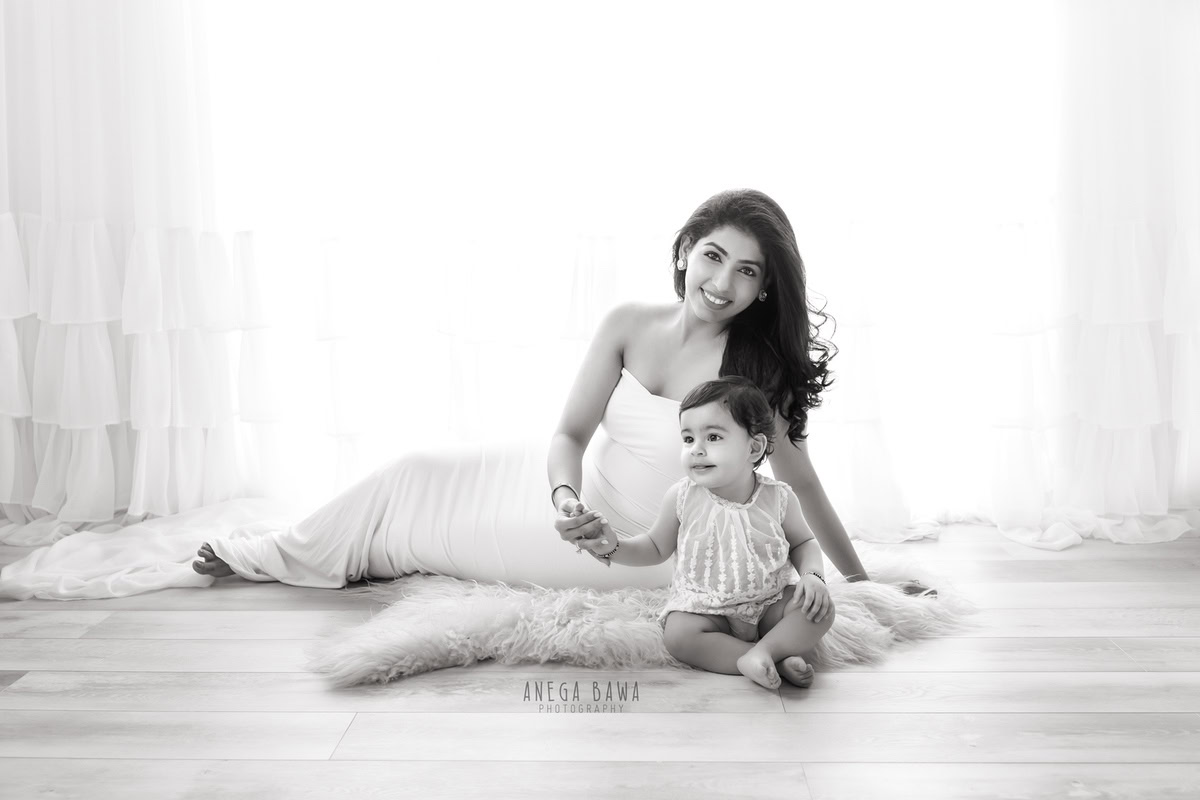 10-month-old girl seated on a beige rug with mom against a clean white backdrop, captured in a serene family portrait by Anega Bawa, Gurgaon (Delhi, NCR)