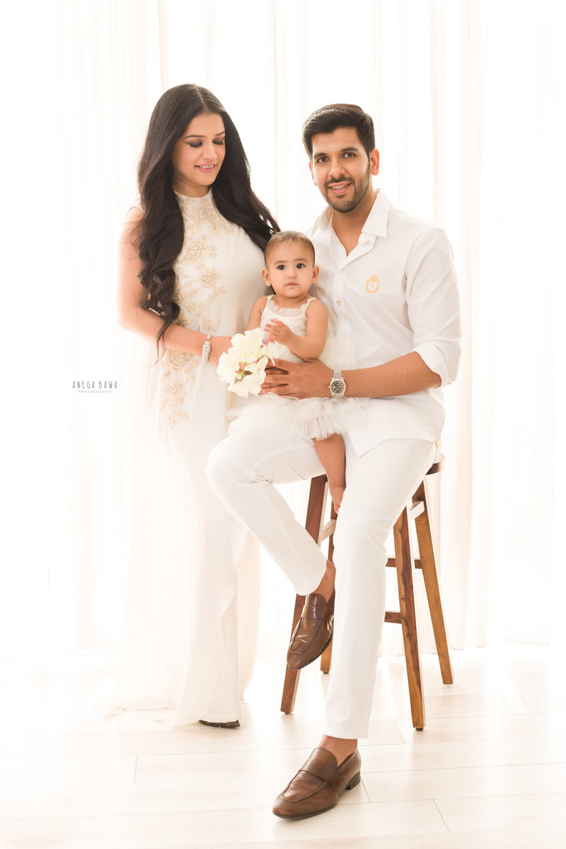 10-months girl seated on dad's lap against a white backdrop, captured by Anega Bawa Family Photographer in Gurgaon (Delhi NCR).
