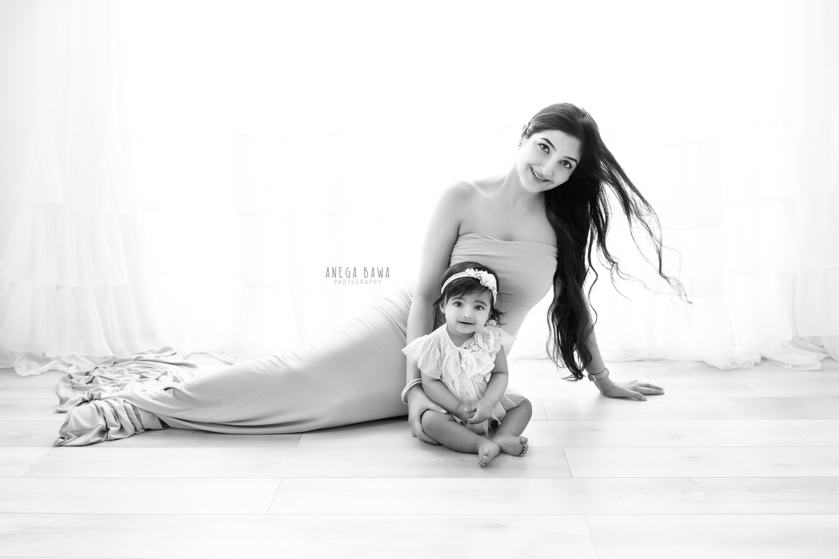 10-month-old girl seated on the floor with mom against a white backdrop, captured in a peaceful family portrait by Anega Bawa, Gurgaon (Delhi, NCR)