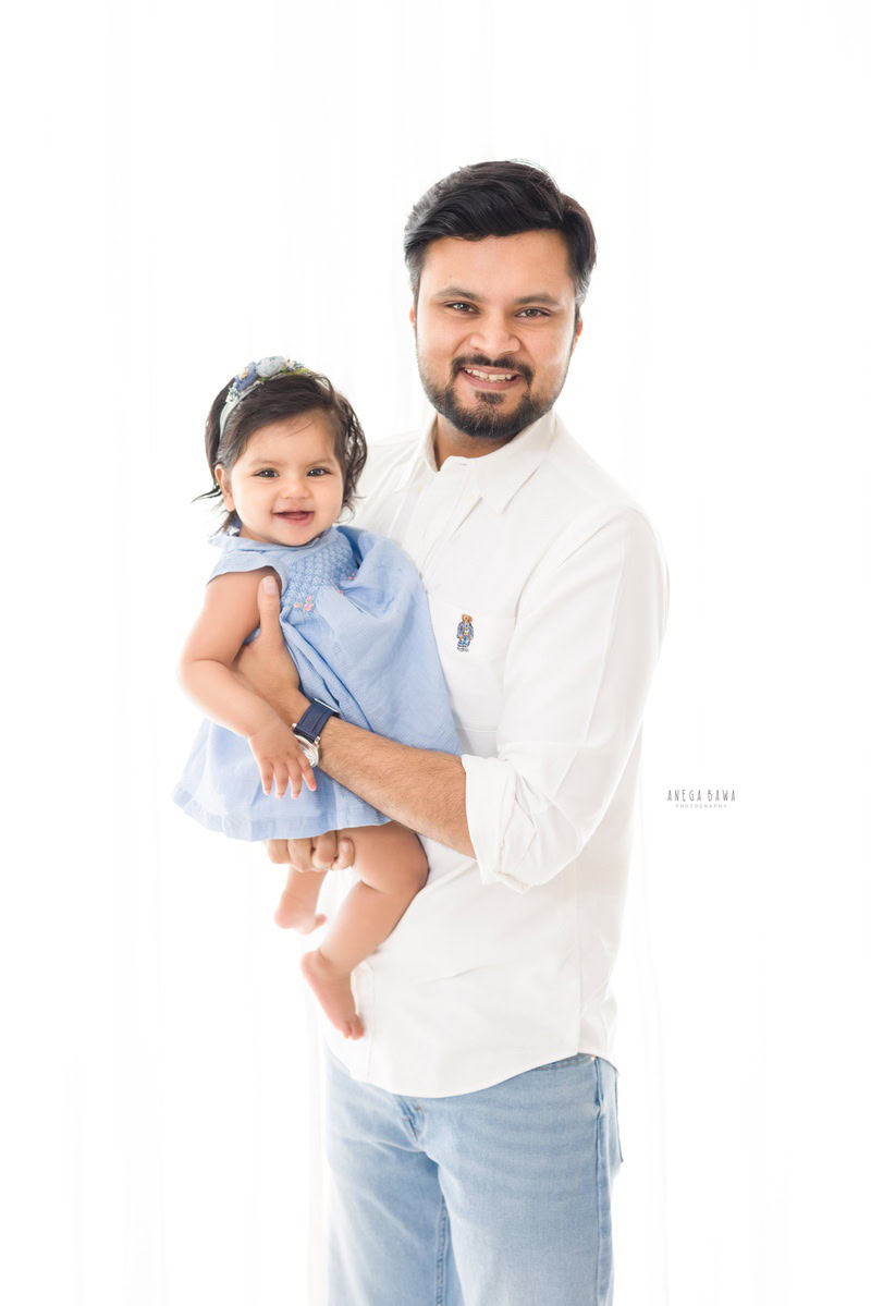 10-month-old girl smiling and posing with dad against a white backdrop, captured by Anega Bawa family photographer Gurgaon (Delhi NCR).