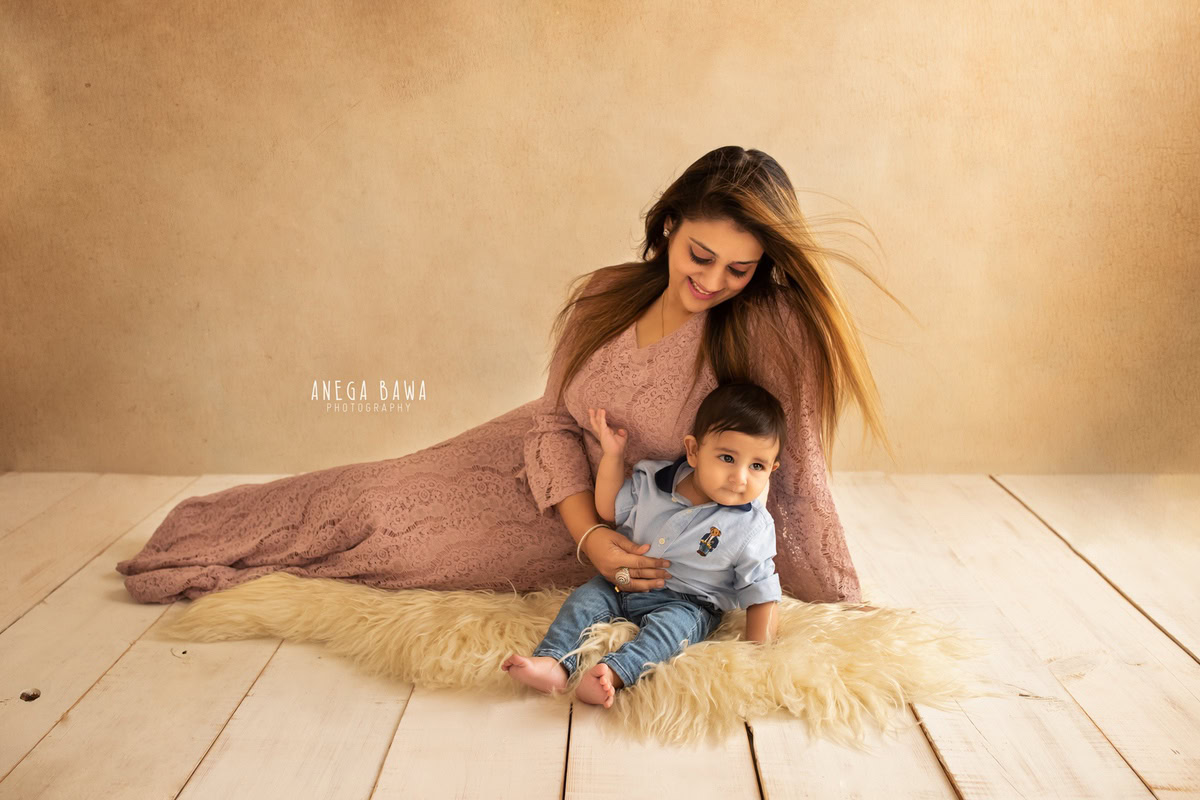 11-month-old boy seated on a beige rug, posing with mom against a matching beige backdrop, captured by Anega Bawa in Gurgaon (Delhi, NCR)
