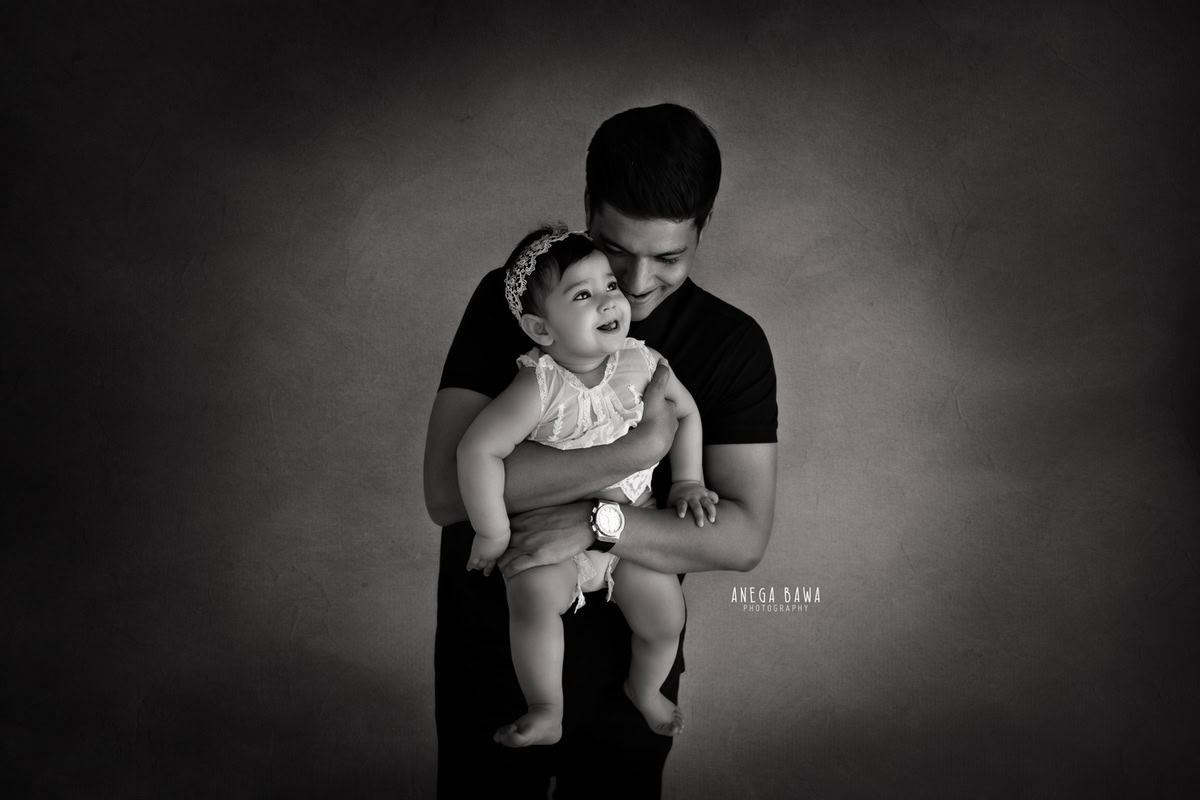 11-month-old girl posing cutely with dad against a black and white backdrop, captured by Anega Bawa in Gurgaon (Delhi, NCR)
