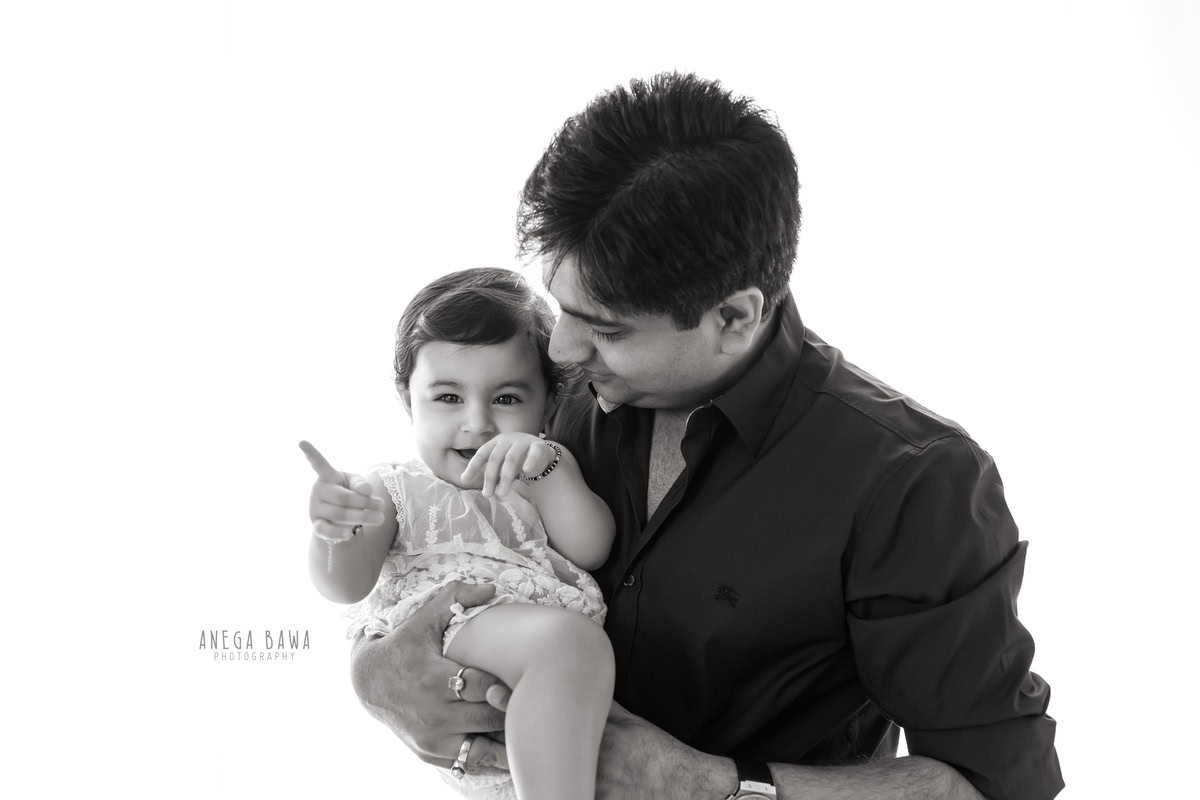 11-month-old girl posing in dad's arms against a white backdrop. Captured by Anega Bawa family photographer Gurgaon (Delhi NCR).