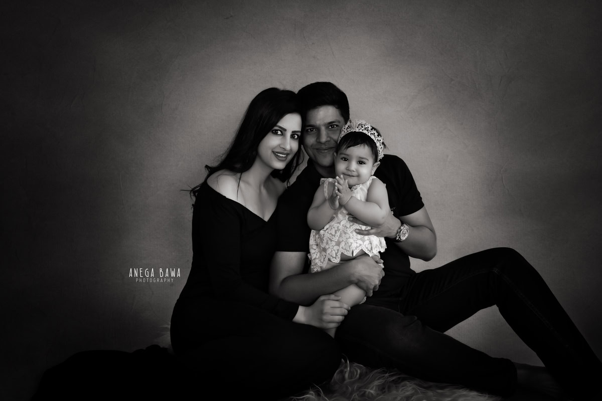 11-month-old girl posing with mom and dad against a black and white backdrop, wearing a cute headband, captured by Anega Bawa in Gurgaon (Delhi, NCR)