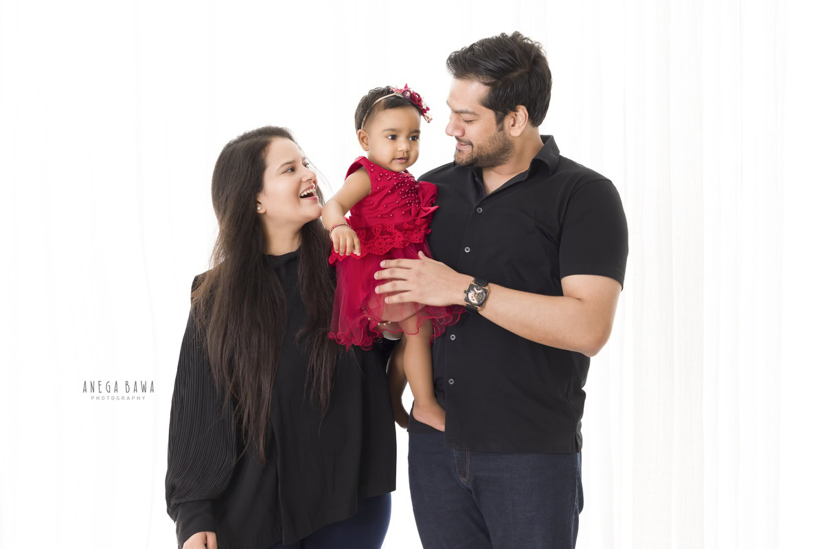 11-month-old girl elegantly posing with mom and dad against a pristine white backdrop. Professionally captured by Anega Bawa Photography, Gurgaon (Delhi NCR).
