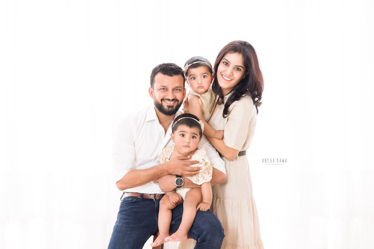 11-month-old twin girls posing cutely with mom and dad, wearing cute headbands, against a white backdrop, captured by Anega Bawa in Gurgaon (Delhi, NCR)