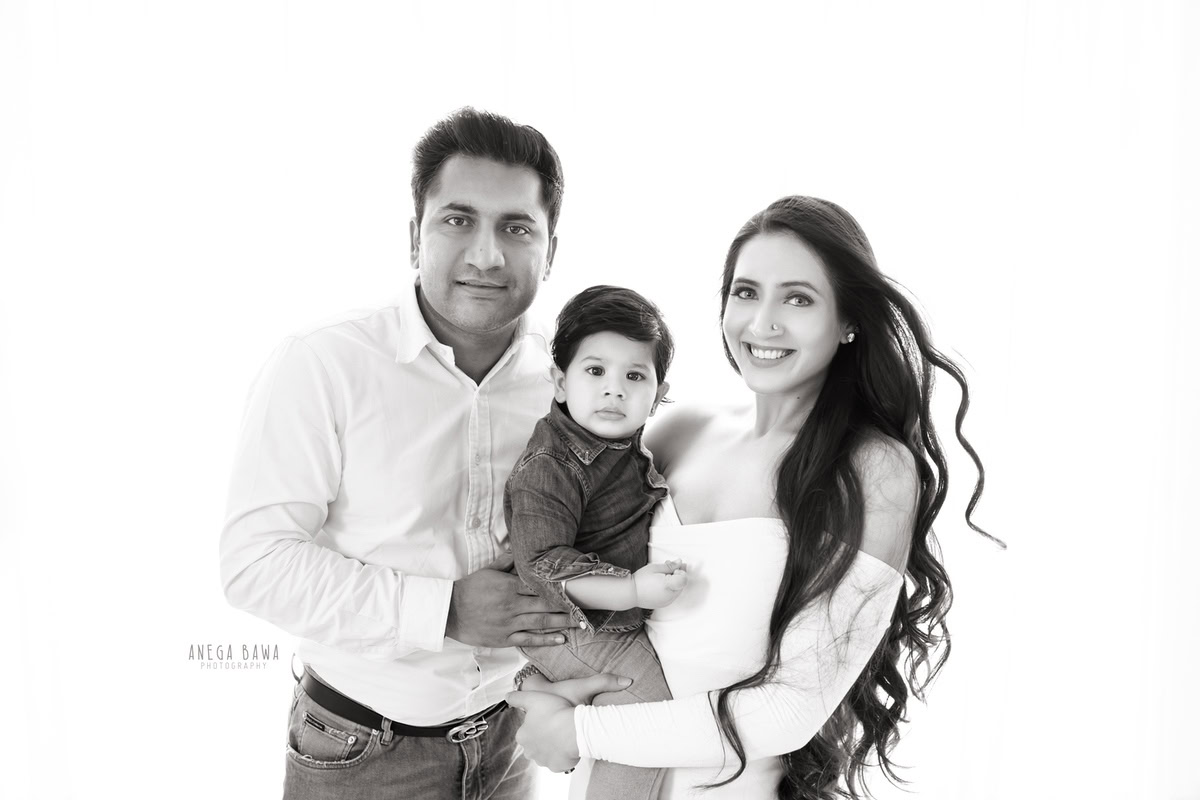 Charming 12-month-old boy posing with loving mom and dad against a pristine white backdrop, beautifully captured by Anega Bawa in Gurgaon (Delhi, NCR)