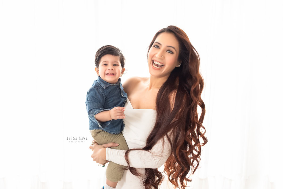 12-month-old boy smiling with mom against a white backdrop, captured by Anega Bawa family photographer Gurgaon (Delhi NCR).