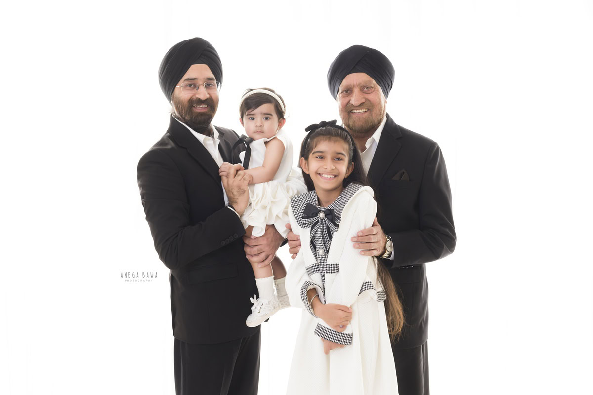 12-month-old girl posing with dad, elder sister, and grandfather against a clean white backdrop, beautifully photographed by Anega Bawa in Gurgaon (Delhi, NCR)