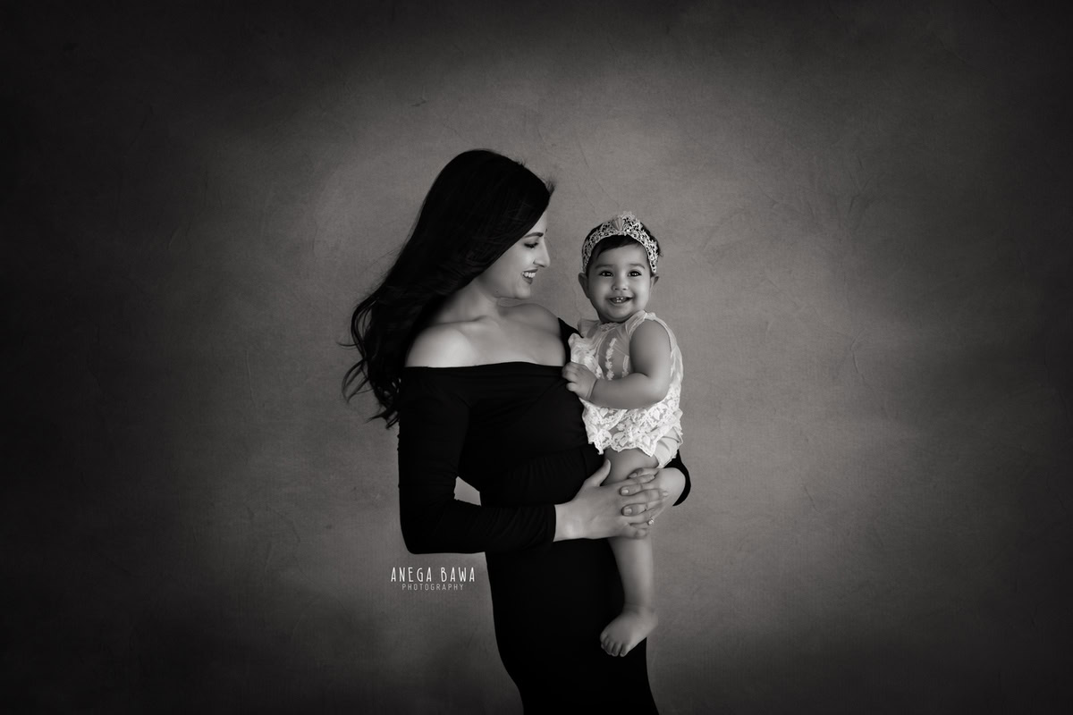 12-month-old girl posing with mom, wearing a cute headband, against a black and white backdrop, photographed by Anega Bawa in Gurgaon (Delhi, NCR)