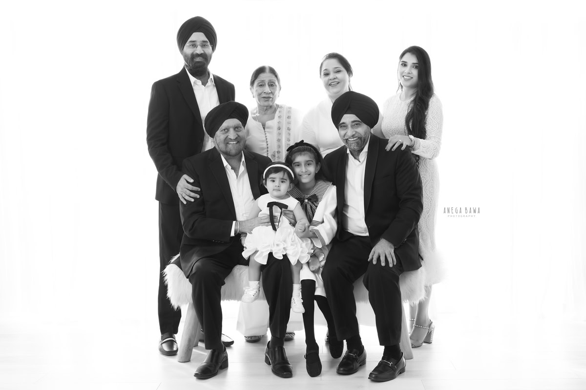 12-month-old girl seated on grandfather's lap, posing with family against a white backdrop, photographed by Anega Bawa in Gurgaon (Delhi, NCR)