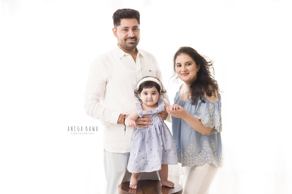 12-month-old girl standing on a stool, wearing a cute headband, against a white backdrop, photographed by Anega Bawa in Gurgaon (Delhi, NCR)