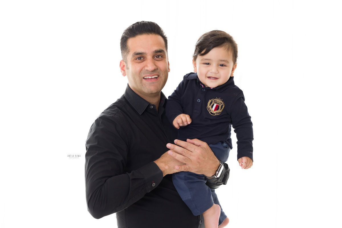 Charming 14-month-old boy posing with dad, who is wearing a black shirt, against a crisp white backdrop, captured by Anega Bawa Family Photographer Gurgaon (Delhi NCR).