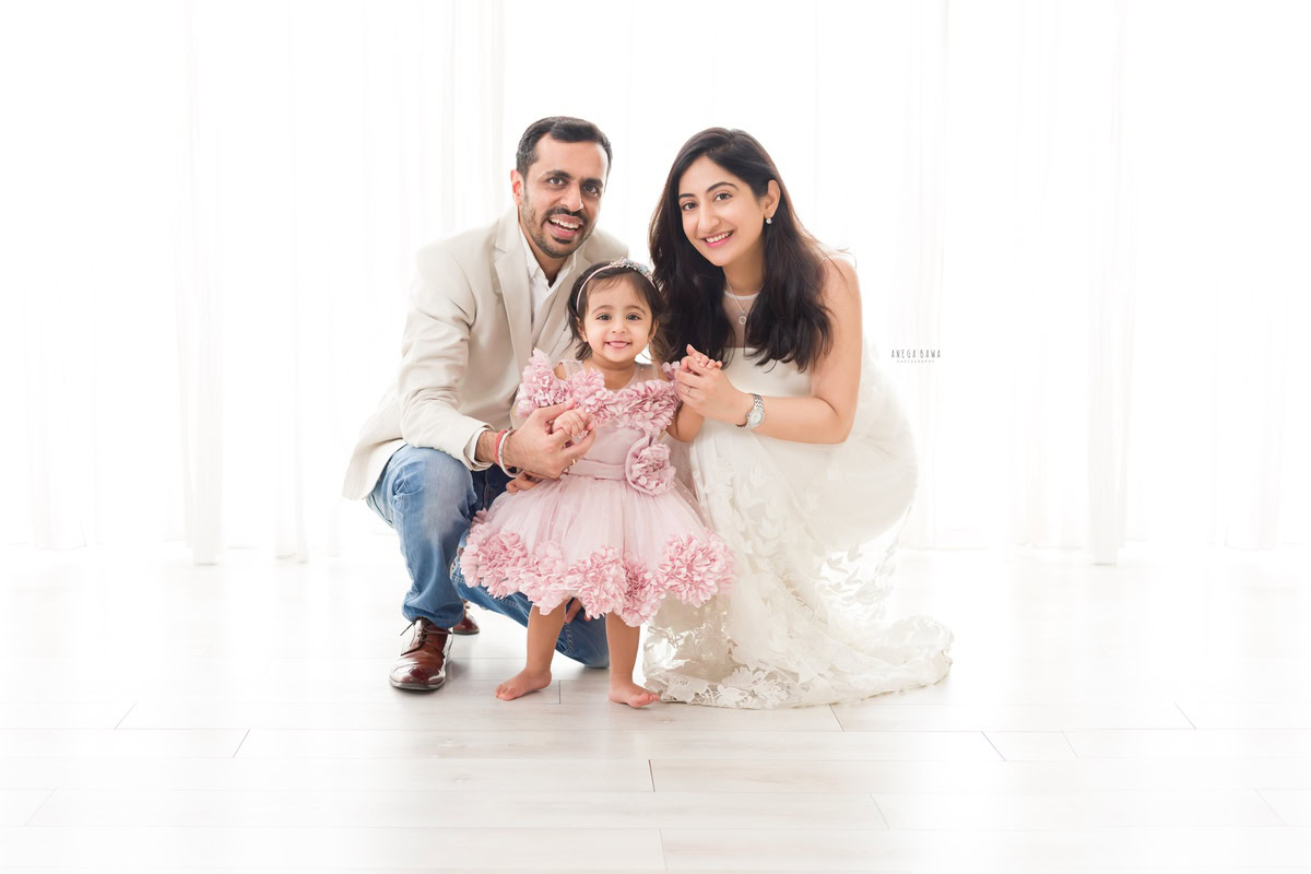 14-month-old girl standing on floor, posing with mom and dad against a white backdrop, captured by Anega Bawa family photographer Gurgaon (Delhi NCR).