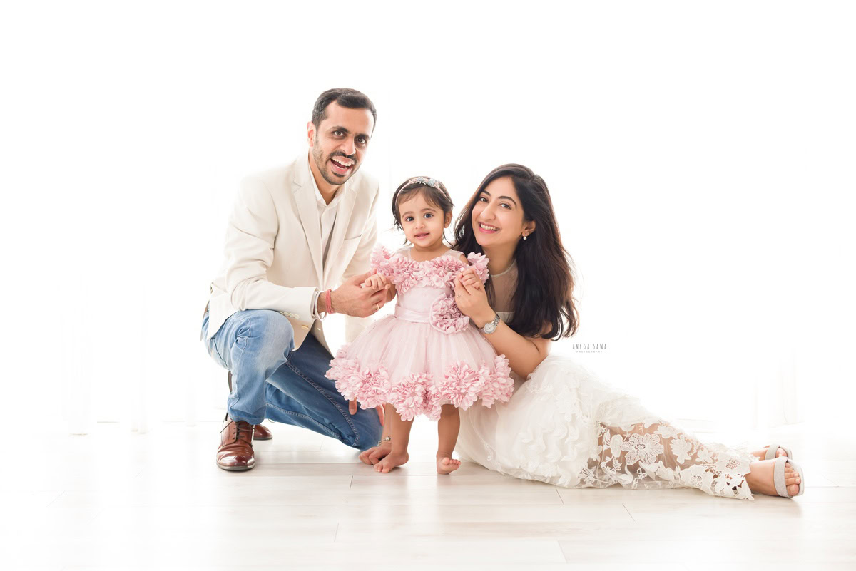 14-month-old girl standing on the floor with mom and dad against a white backdrop, captured by Anega Bawa family photographer Gurgaon (Delhi NCR).