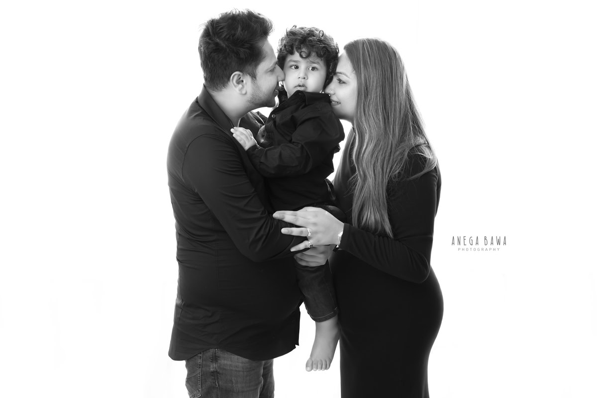 15-month-old boy posing with mom and dad, all wearing black, against a white backdrop, captured by Anega Bawa family photographer Gurgaon (Delhi NCR).