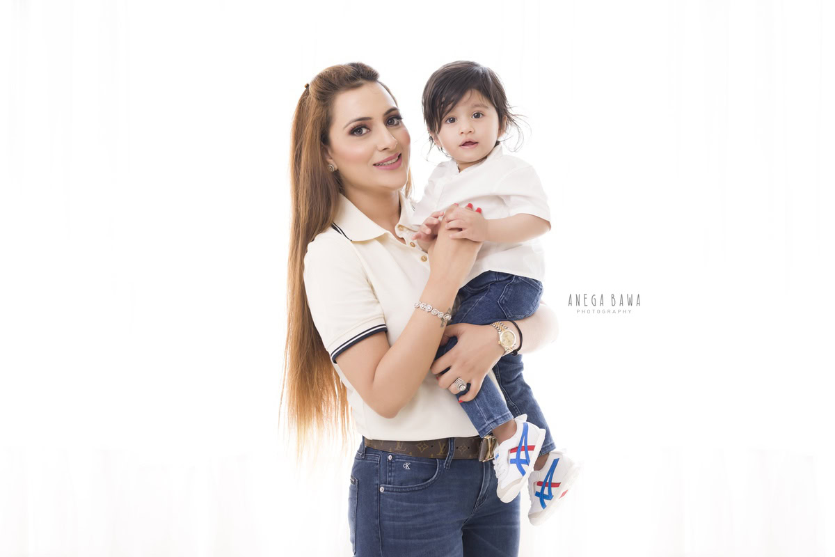 15-month-old boy posing with mom, both twinning in white tees against a white backdrop. This adorable moment was captured by Anega Bawa Photography for a family photoshoot in Gurgaon (Delhi NCR).