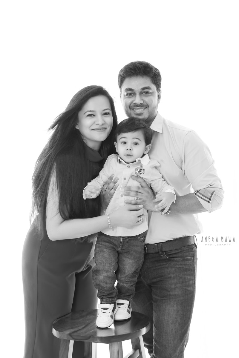 Adorable 15-month-old boy standing on a stool, posing with mom and dad against a clean white backdrop, captured by Anega Bawa Family Photographer Gurgaon (Delhi NCR).