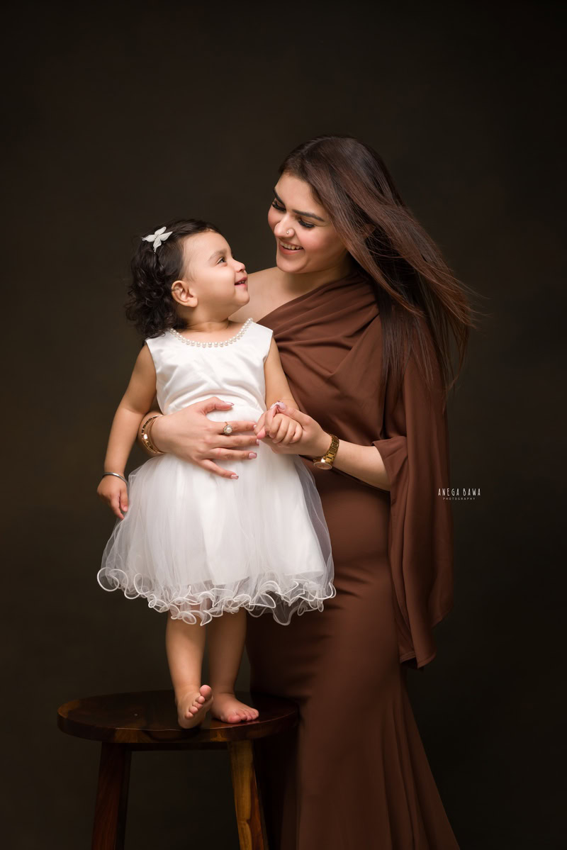 15-month-old girl in an eye-to-eye pose with mom against a brown backdrop, photographed by Anega Bawa in Gurgaon (Delhi, NCR)