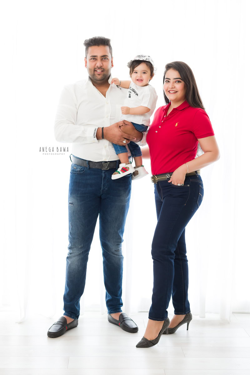 15-month-old girl wearing a cute headband, posing with mom and dad against a white backdrop, captured by Anega Bawa family photographer Gurgaon (Delhi NCR).