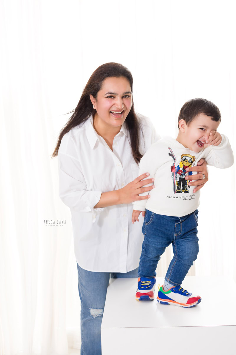 3-year-old boy posing cutely with his mom, both dressed in white, against a serene white backdrop, captured by Anega Bawa Family Photographer in Gurgaon (Delhi NCR).