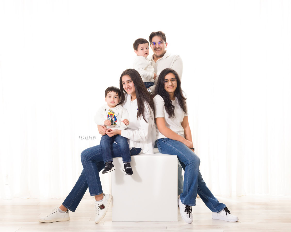 3-year-old boy seated on mom's lap, with dad, elder sister, and brother in a family pose against a white backdrop, captured by Anega Bawa family photographer Gurgaon (Delhi NCR)