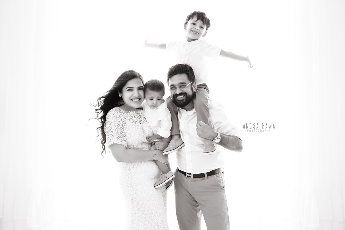 7-month-old son posing with mom, dad, and elder brother against a white backdrop, captured by Anega Bawa Photography for a family photoshoot in Gurgaon (Delhi NCR).