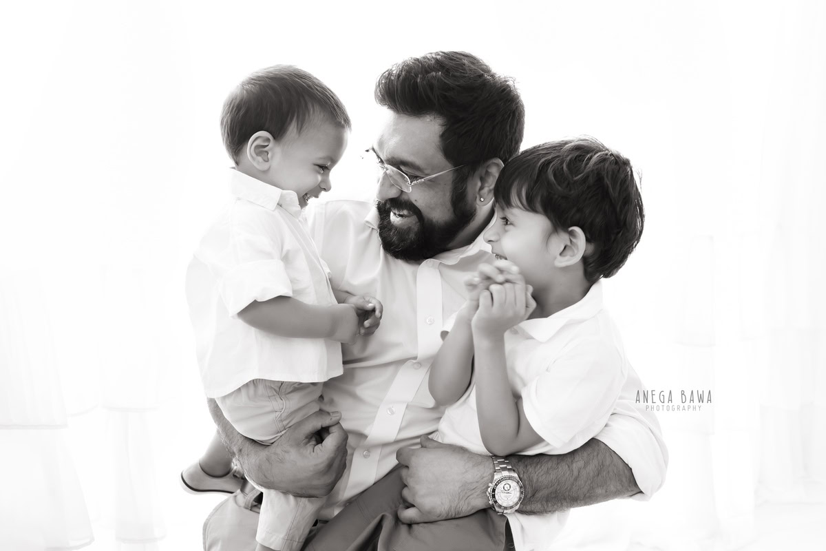 7-month-old son posing with dad and elder brother against a neutral white backdrop. Captured by Anega Bawa Photography, Gurgaon (Delhi, NCR).