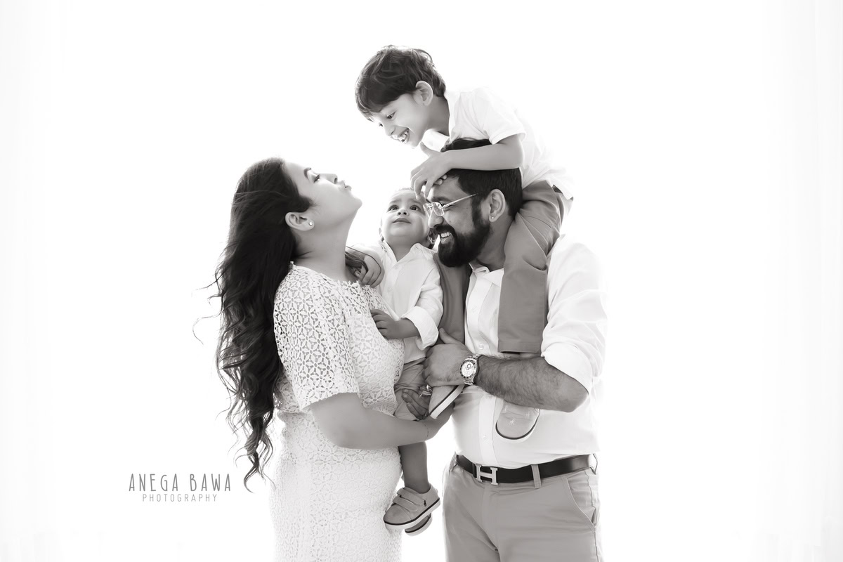 7-month-old son posing with his mom, dad, and elder brother against a serene white backdrop, captured by Anega Bawa Photography for a family photoshoot in Gurgaon (Delhi NCR).