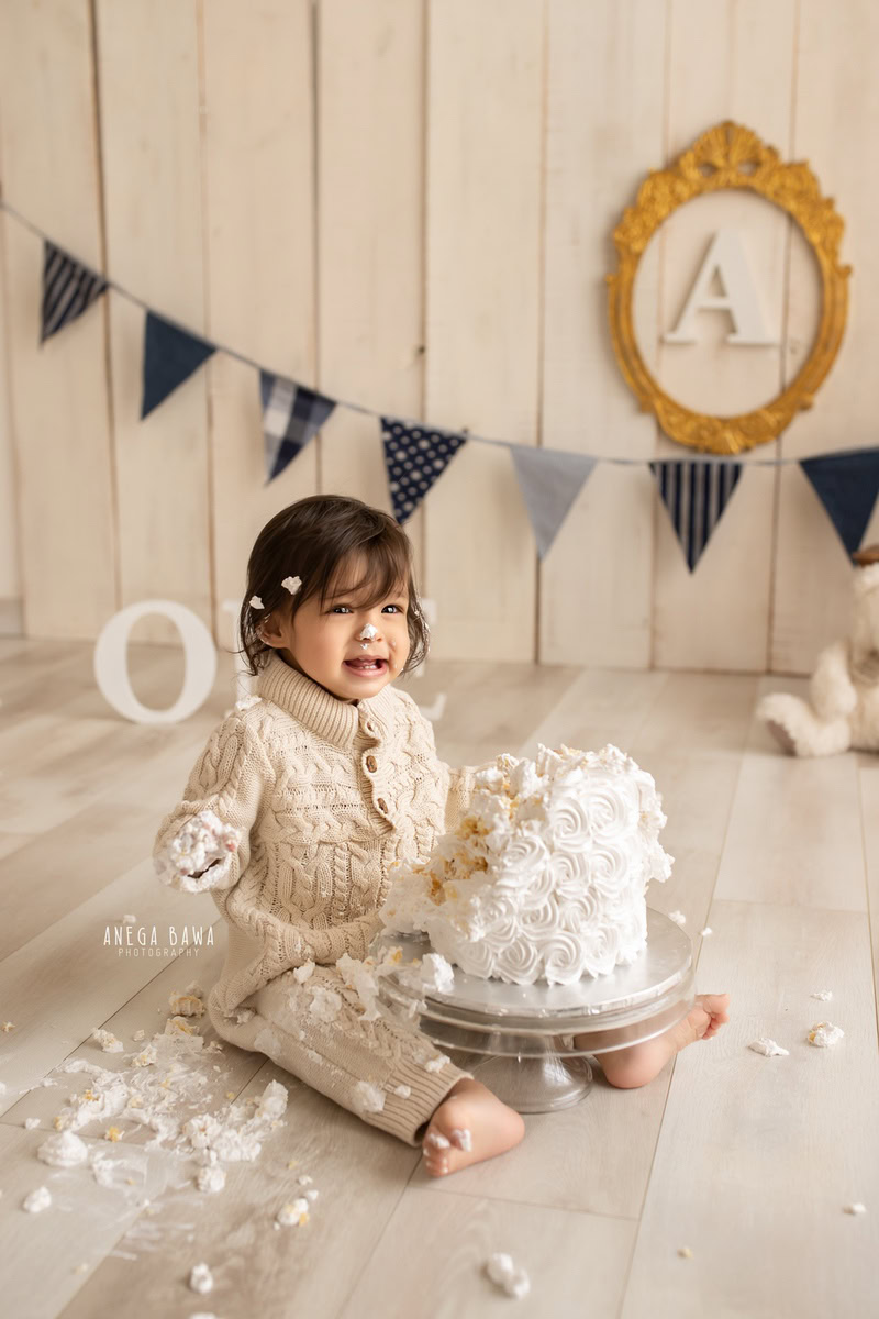 1year old boy enjoying a cake smash with a beige backdrop and adorable teddybears. Captured in a captivating first birthday photo shoot in Delhi, Gurgaon by the renowned family photographer Anega Bawa.