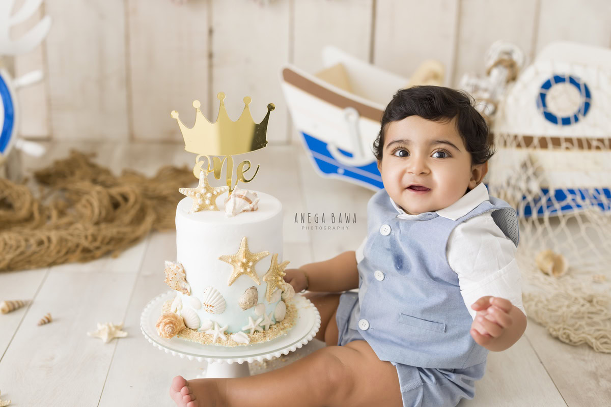 1 year old boy Cake Smash first birthday photoshoot in Delhi, Gurgaon with toy spaceship and beige backdrop. Captured by Anega Bawa family photographer Gurgaon (Delhi NCR)