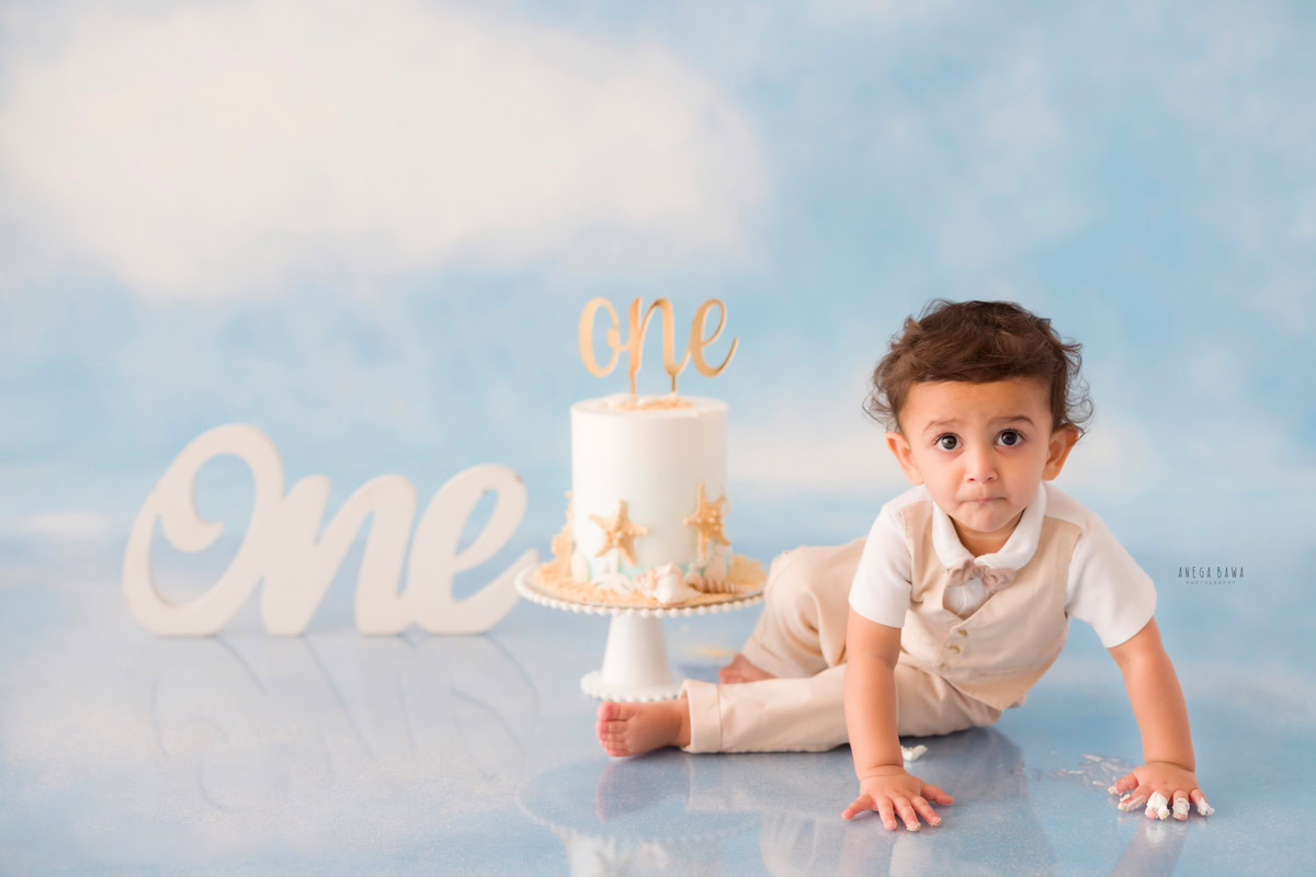 1 year boy with a cake, set against a cloudy backdrop during a first birthday photoshoot by well-known Anega Bawa Photography in Delhi, Gurgaon.
