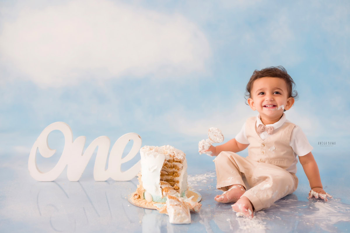 1 year boy with cake on his face, set against a cloudy backdrop during a first birthday photoshoot by well-known Anega Bawa Photography in Delhi, Gurgaon.