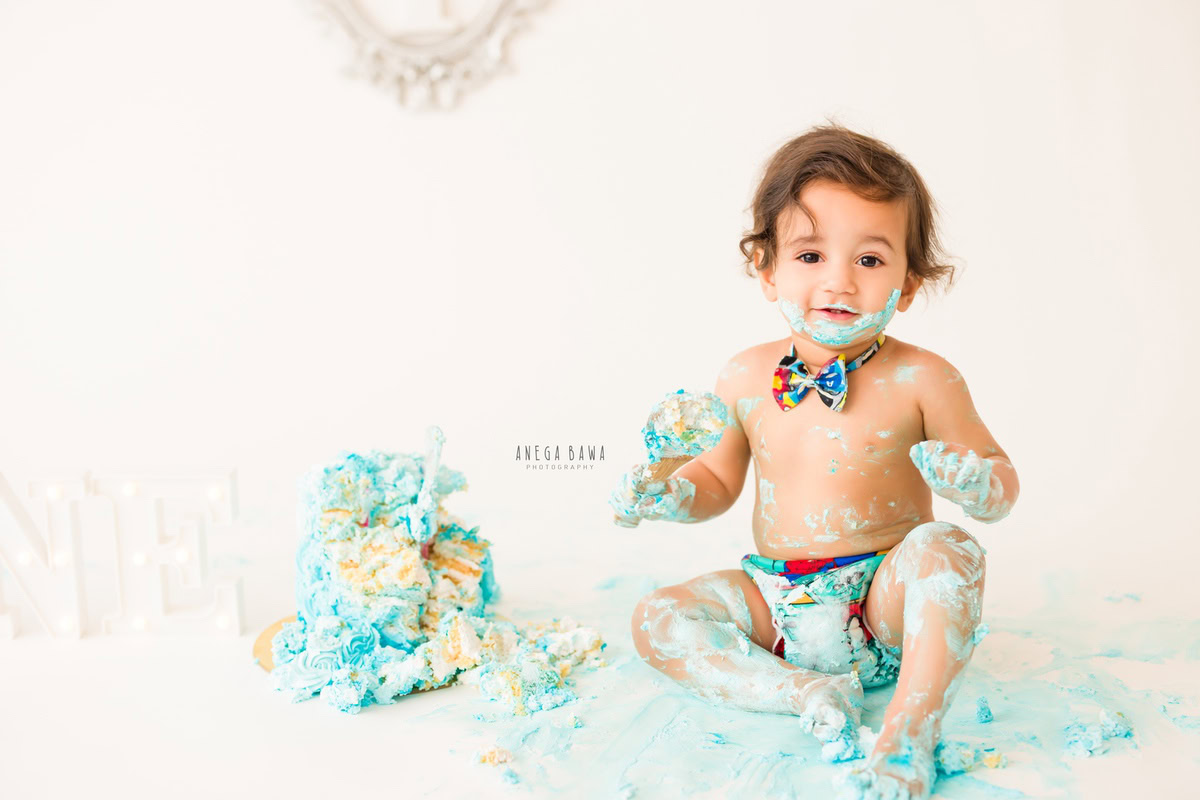 1year old boy with cake smash white backdrop and a cute bow. Captured during an adorable first birthday photoshoot in Delhi Gurgaon by the esteemed family photographer Anega Bawa.