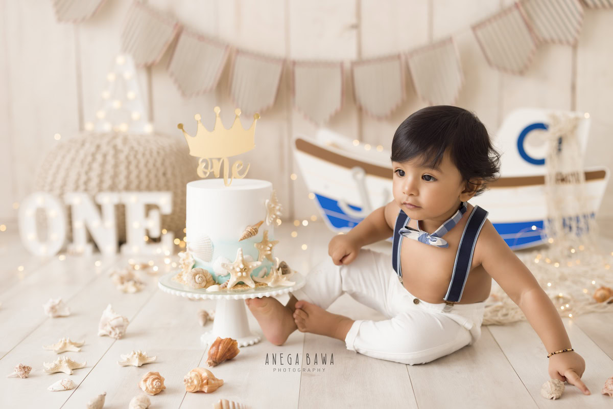 1 year old boy Cake Smash first birthday photoshoot in Delhi, Gurgaon with toy spaceship, beige backdrop, and fairy lights. Captured by Anega Bawa family photographer Gurgaon (Delhi NCR