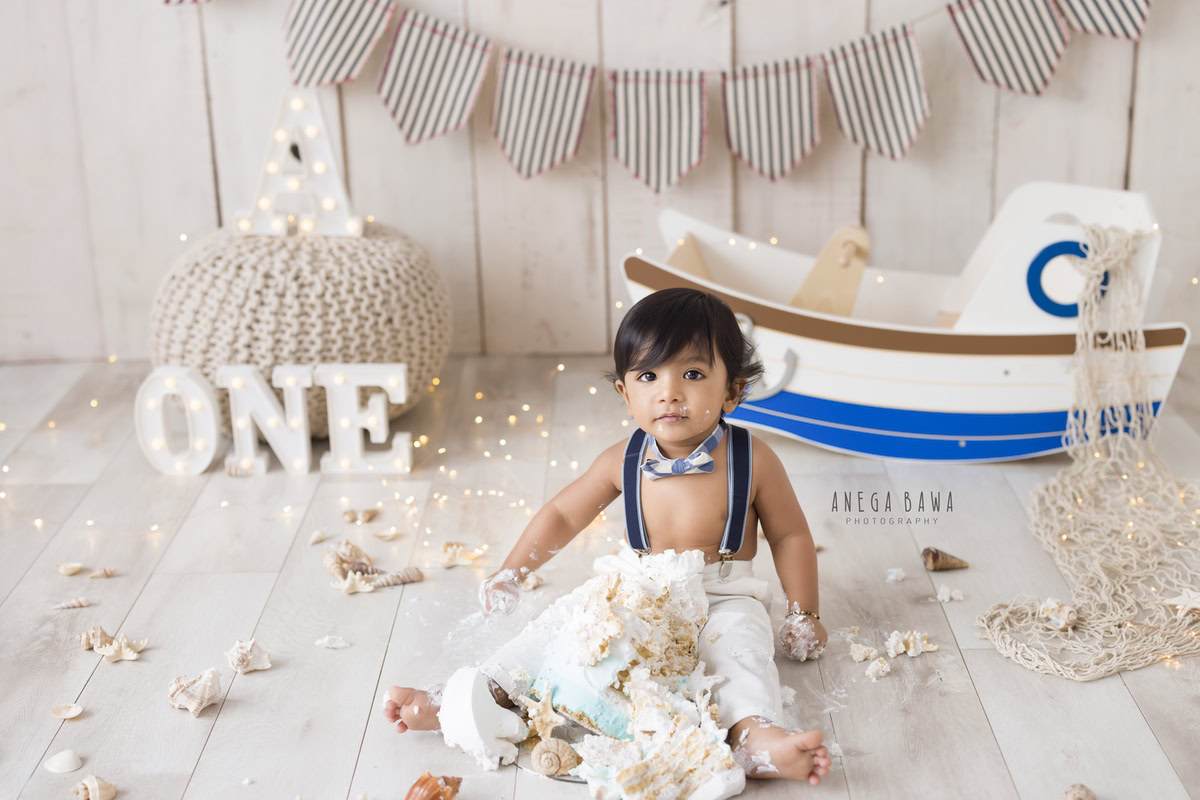 1 year old boy Cake Smash first birthday photography in Delhi, Gurgaon with toy spaceship and beige backdrop. Captured by Anega Bawa family photographer Gurgaon (Delhi NCR)