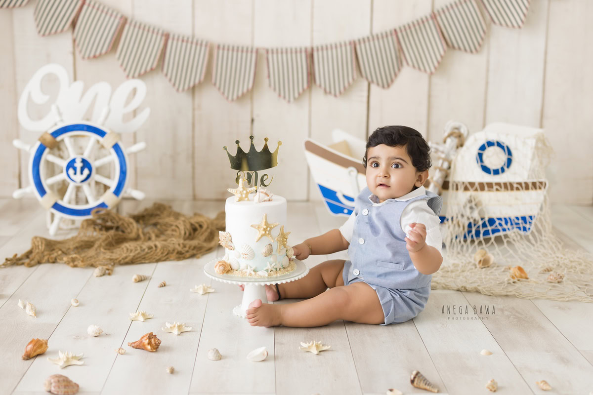 1 year old boy with Cake Smash, featuring a toy spaceship and petals on the floor against a beige backdrop, captured in a delightful first birthday photo shoot by Anega Bawa in Delhi, Gurgaon.