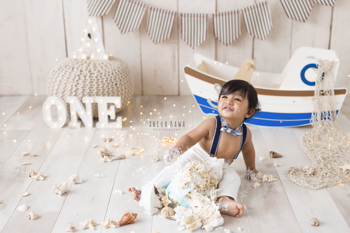 1year old boy with cake smash toy spaceship fairy lights and beige backdrop. Captured during a fun first birthday photography session in Delhi Gurgaon by the well-known family photographer Anega Bawa.