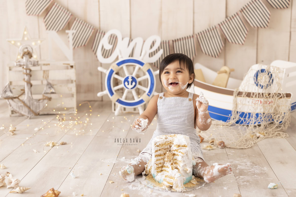 1 year boy with a cake, surrounded by a toy spaceship and fairy lights against a beige backdrop during a first birthday photography session by well-known Anega Bawa Photography in Delhi, Gurgaon.