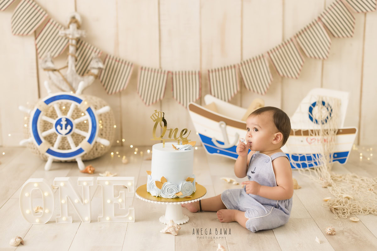 1year old boy with a toy spaceship and fairy lights, enjoying a cake smash session with a beige backdrop. Celebrating his first birthday. Cake Smash photo shoot in Delhi, Gurgaon by Anega Bawa Family Photographer Gurgaon (Delhi NCR).