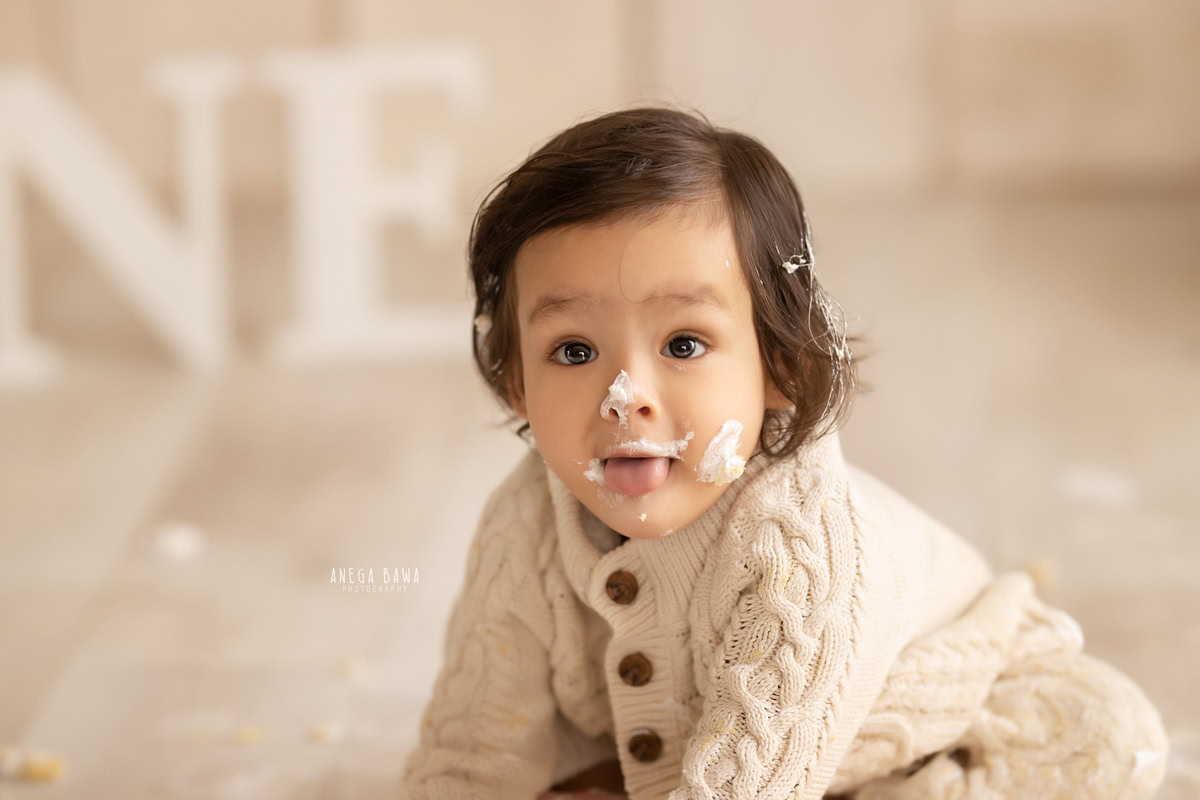 1 year old boy crawling Cake Smash on face first birthday photoshoot in Delhi, Gurgaon with beige backdrop. Captured by Anega Bawa family photographer Gurgaon (Delhi NCR)