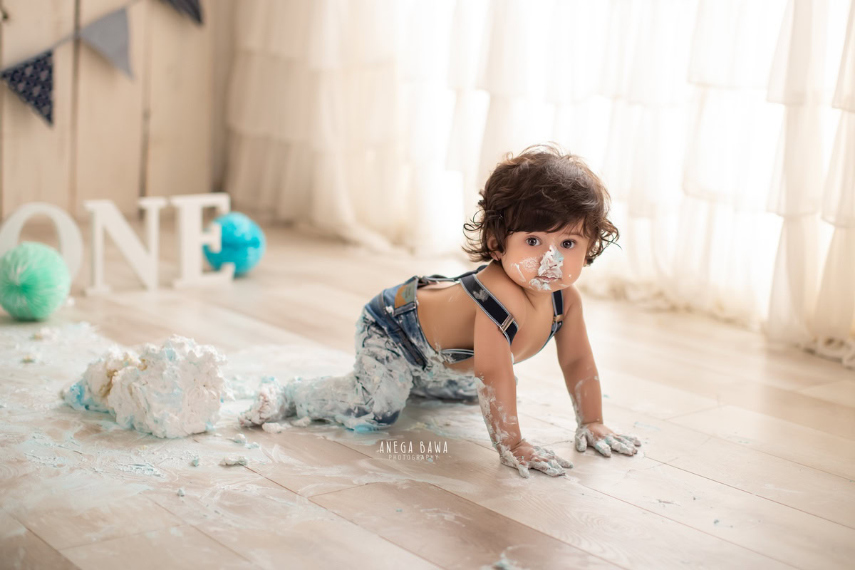 1 year old boy crawling on floor Cake Smash on face first birthday photoshoot in Delhi, Gurgaon with beige backdrop. Captured by Anega Bawa family photographer Gurgaon (Delhi NCR)