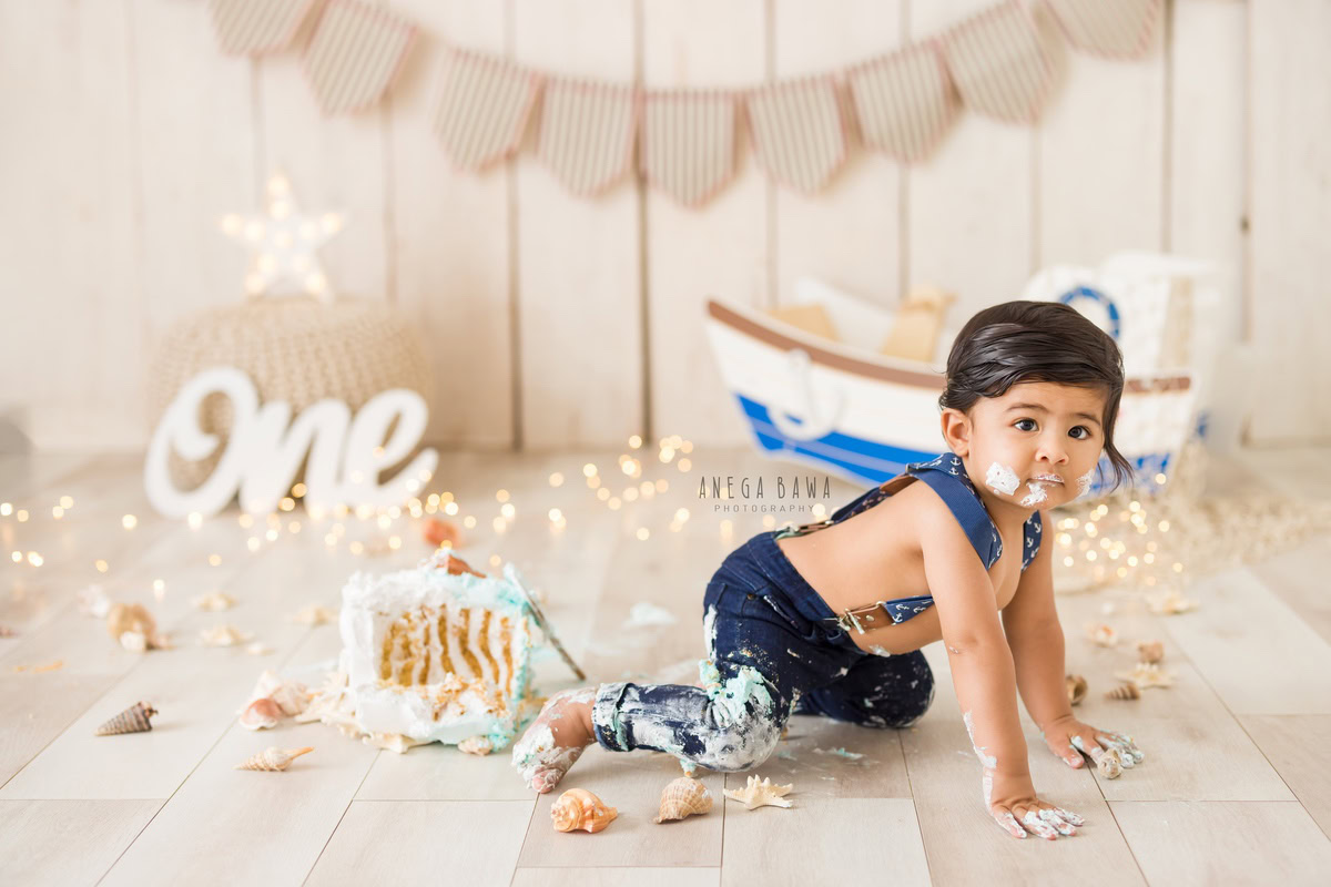 1year old boy crawling on the floor with cake smash fairy lights beige backdrop and toy spaceship. Captured during an engaging first birthday photoshoot in Delhi Gurgaon by the renowned family photographer Anega Bawa.