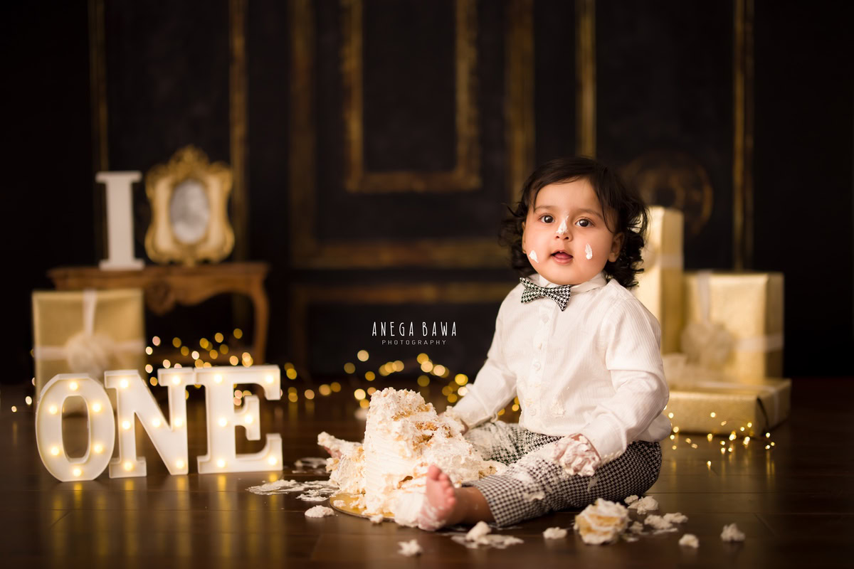 1year old boy with cake smash cute bow brown backdrop and fairy lights. Captured during a memorable first birthday photoshoot in Delhi Gurgaon by the well-known family photographer Anega Bawa.