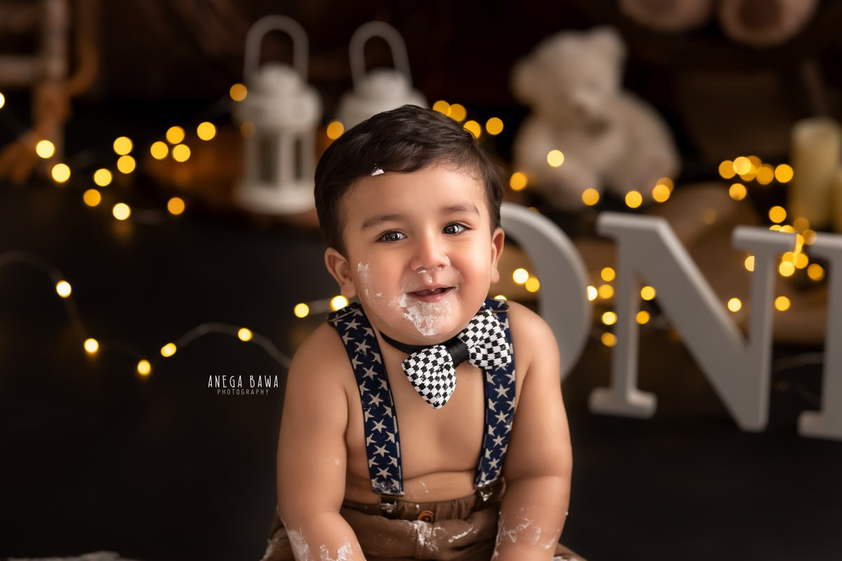 1 year old boy with cute bow, white castles, teddy bears, and fairy lights, brown backdrop, first birthday photo shoot in Delhi, Gurgaon. Captured by Anega Bawa family photographer Gurgaon (Delhi NCR)