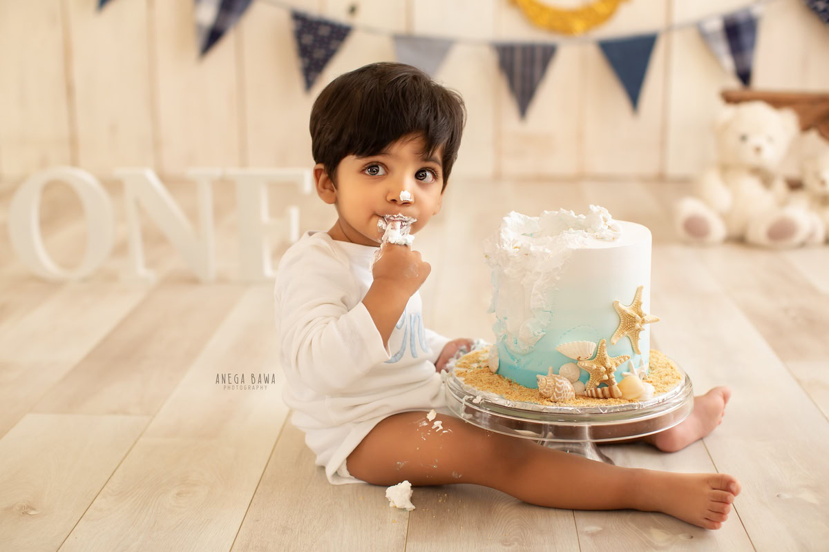 1 year old boy enjoying a cake smash with teddybears against a beige backdrop. Captured during a delightful first birthday photography session in Delhi Gurgaon by the renowned family photographer Anega Bawa.
