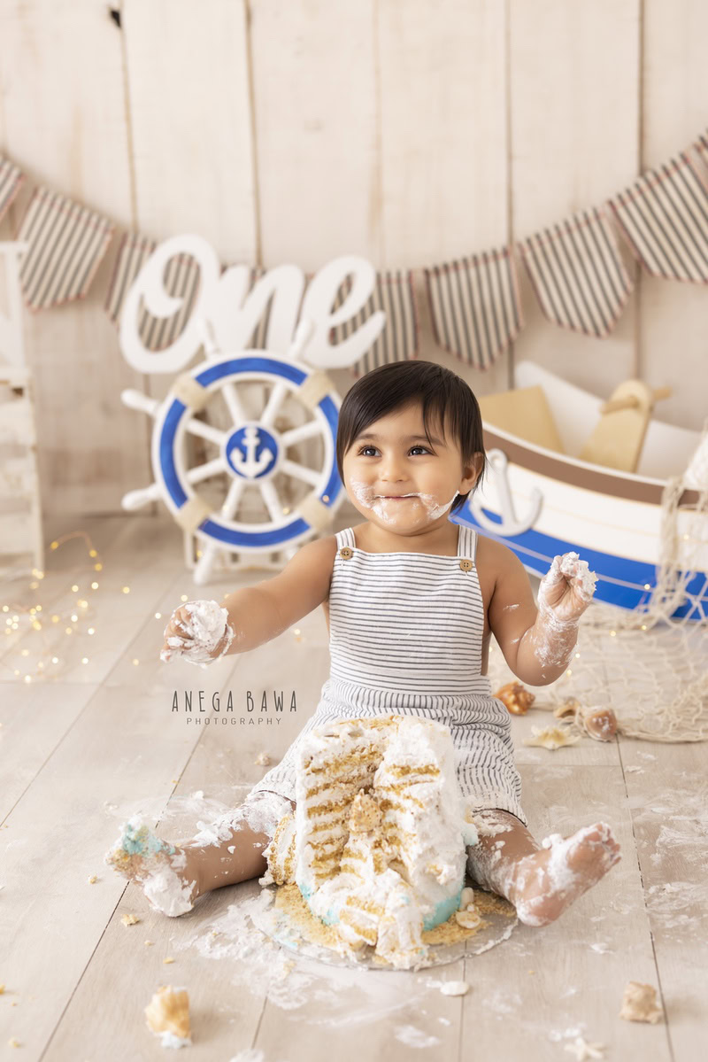 1year old boy playing with a cake smash toy spaceship against a beige backdrop, captured by Anega Bawa during a Cake Smash photoshoot in Delhi, Gurgaon